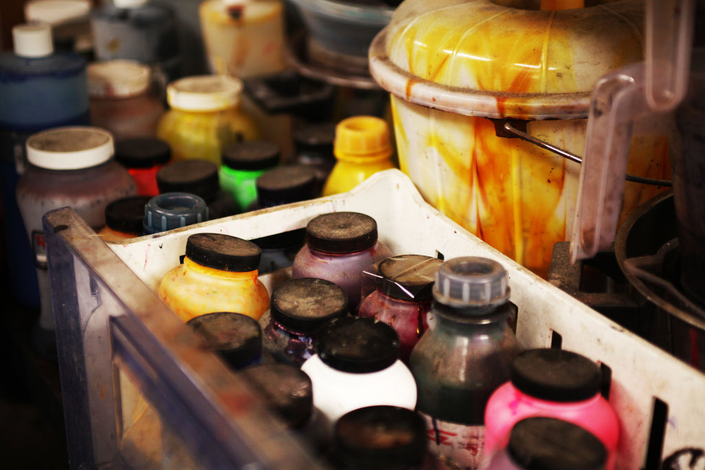 Selection of many paints and pigments in bottles a colourful bucket in the background 